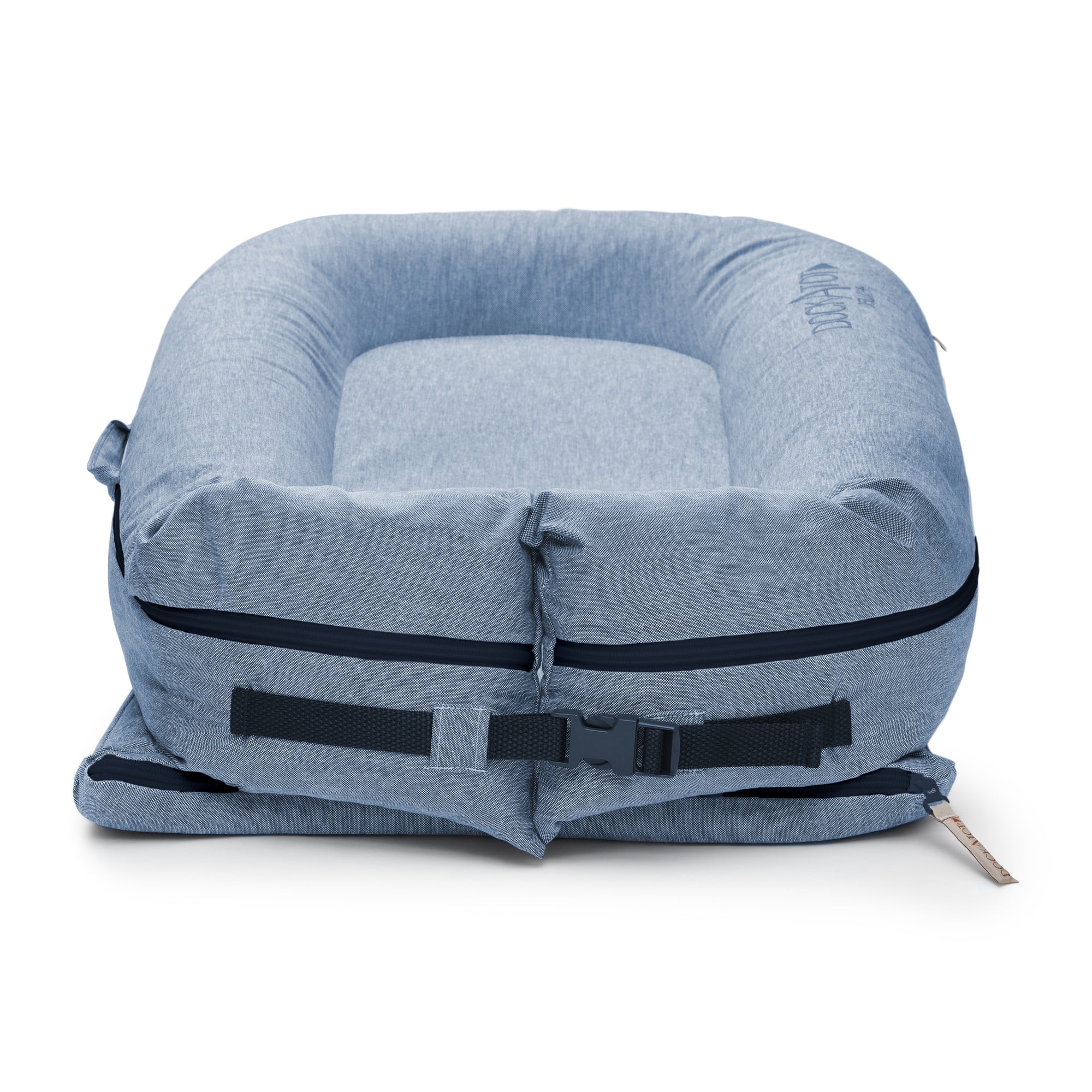 A blue, inflatable travel pillow designed in a U-shape with a zipper and a black adjustable strap. This DockATot Deluxe+ Dock - Indigo Chambray is compact and set against a white background.